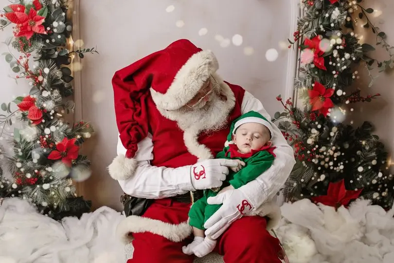 Santa Skip gently holding a sleeping baby dressed in green