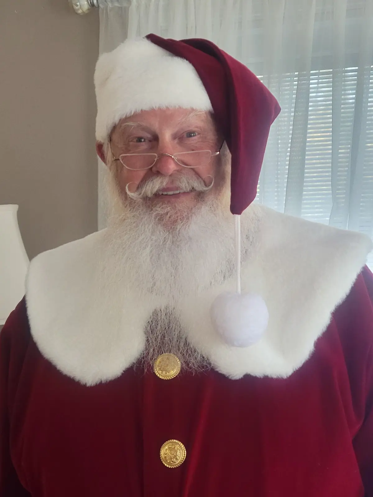 Santa Skip smiling in his traditional Santa suit and signature half-eye glasses